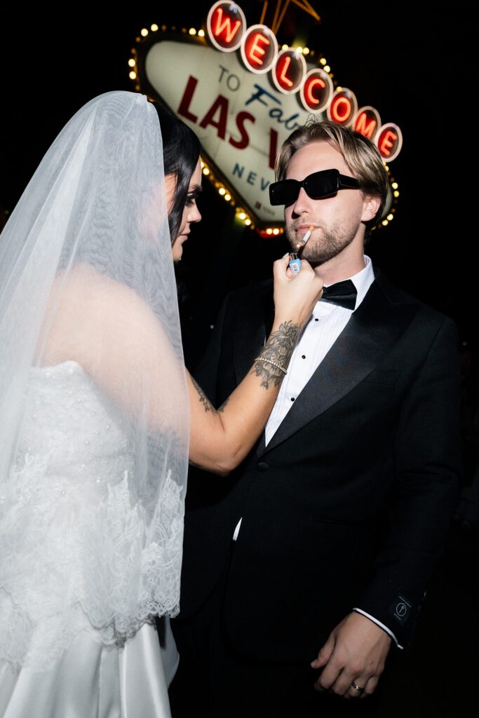 Bride lighting a cigarette for her groom during their Las Vegas Sign wedding photos.