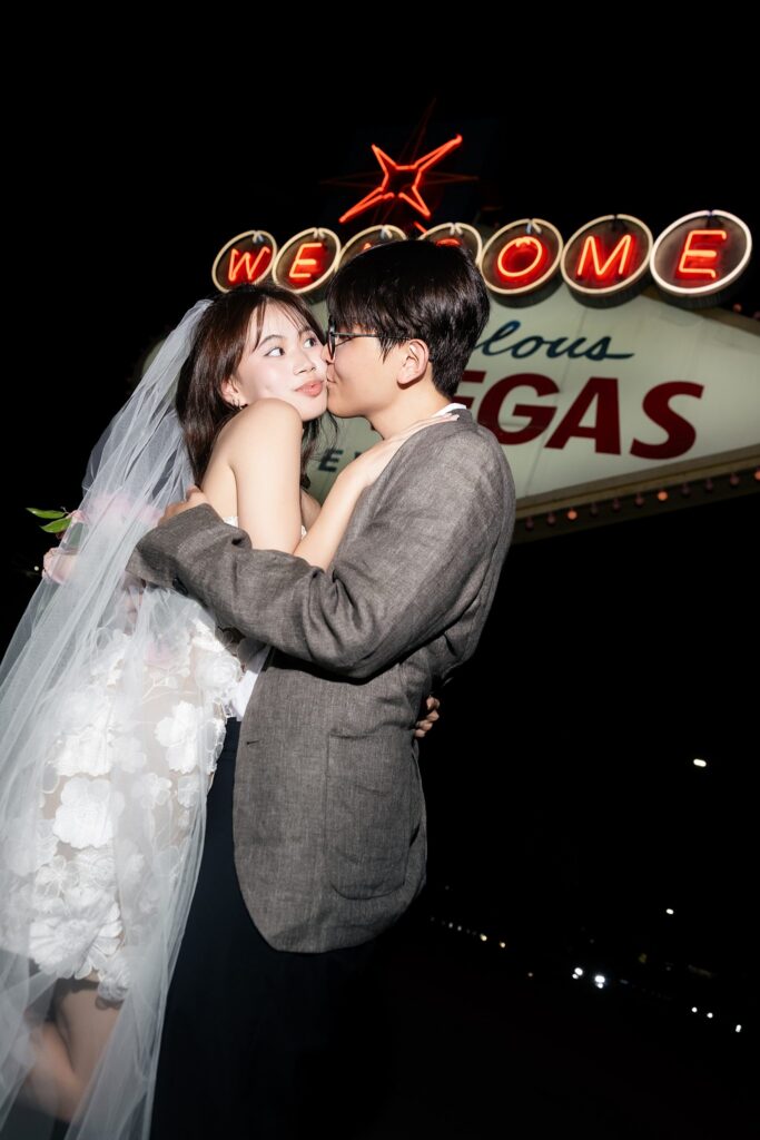 Groom kissing his bride on the cheek during their Las Vegas elopement photos in front of the Welcome to Fabulous Las Vegas sign.