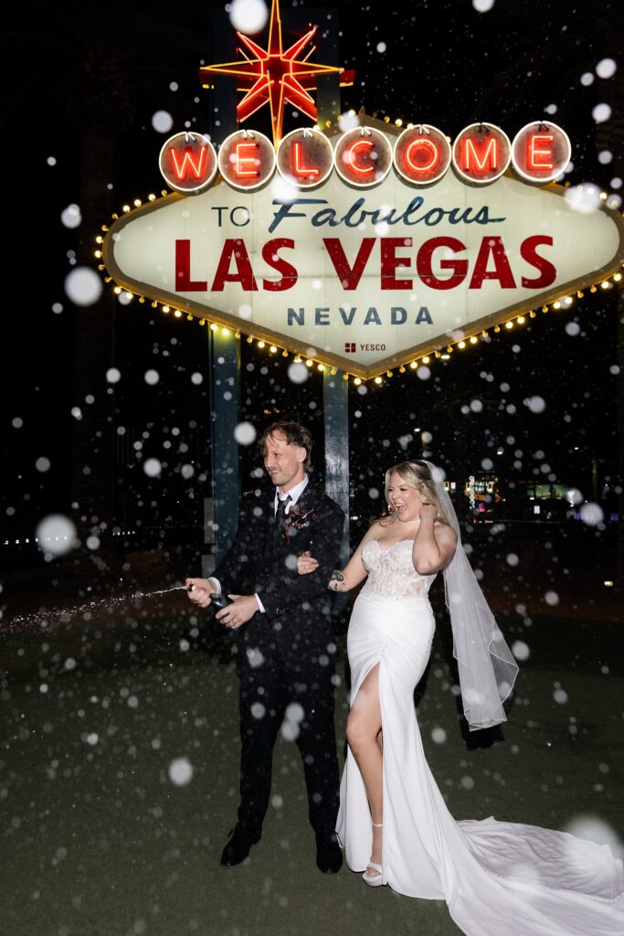 Couple popping champagne at night in front of the Welcome to Fabulous Las Vegas sign.
