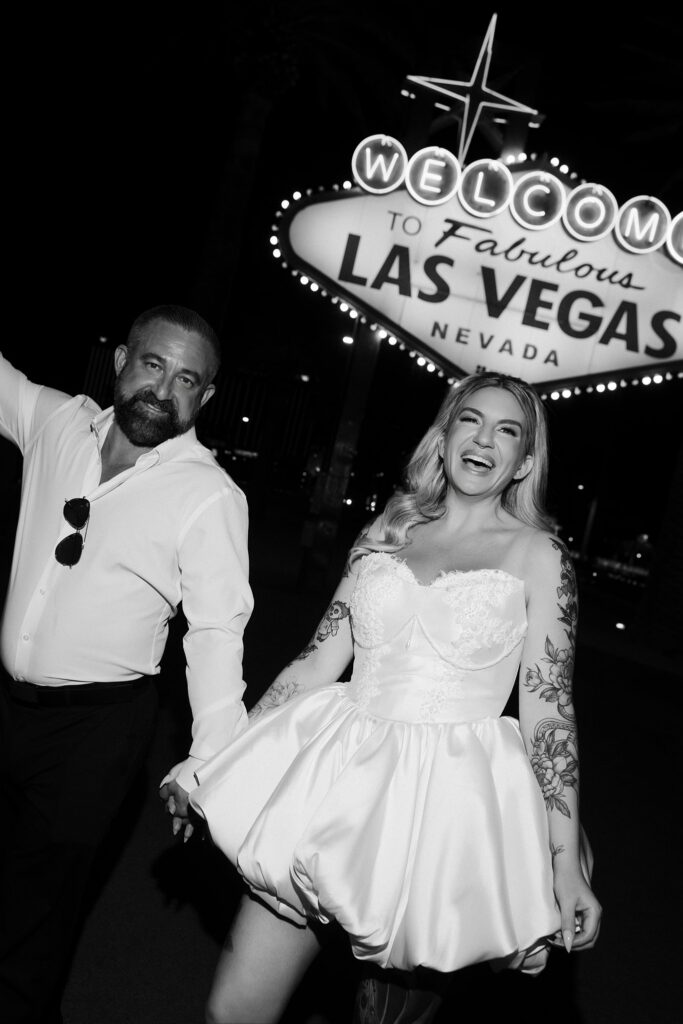 Black and white photo of a couple smiling in front of the Welcome to Fabulous Las Vegas sign for their wedding photos.